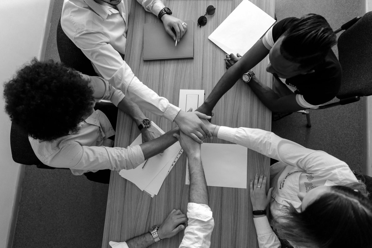 Personas alrededor de una mesa de trabajo uniendo sus manos al centro